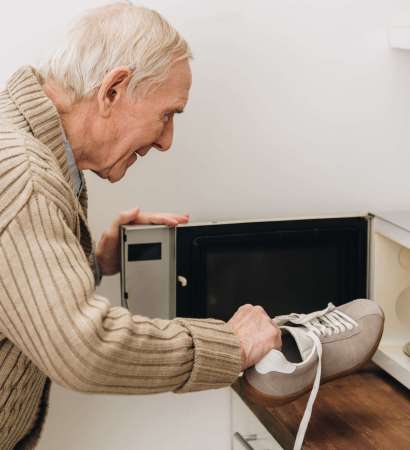 retired man with dementia disease putting shoe in microwave oven